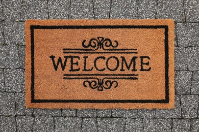 Photo of Doormat with word Welcome on pavement outdoors, top view