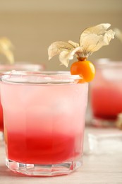 Photo of Refreshing cocktail decorated with physalis fruit on wooden table, closeup