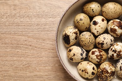 Bowl with quail eggs on wooden table, top view. Space for text