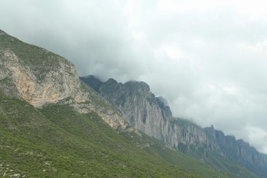 Picturesque landscape with high mountains and fog under cloudy sky