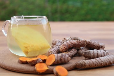 Photo of Glass cup of hot tea and fresh turmeric roots on wooden table, closeup