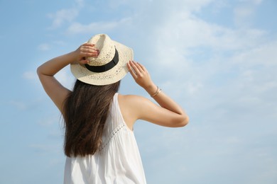 Beautiful young woman wearing straw hat outdoors, back view. Stylish headdress