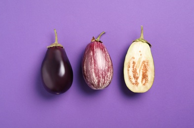 Cut and whole raw ripe eggplants on violet background, flat lay