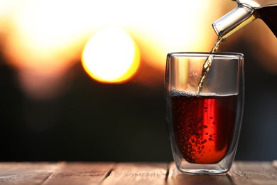 Pouring delicious tea into glass on wooden table against blurred background, closeup. Space for text