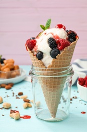 Delicious ice cream with berries in wafer cone served on light blue table