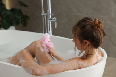 Photo of Beautiful woman with mesh pouf taking bath indoors