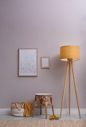 Wooden stool, lamp and bag near light grey wall indoors. Interior accessories