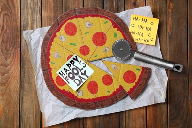 Cardboard pizza and Happy Fools' Day note on wooden table, flat lay