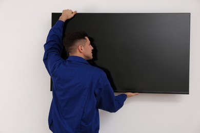 Professional technician installing modern flat screen TV on wall indoors