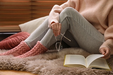 Woman in knitted socks reading book on floor at home, closeup