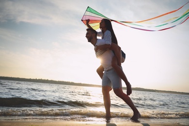 Happy couple playing with kite on beach near sea at sunset. Spending time in nature
