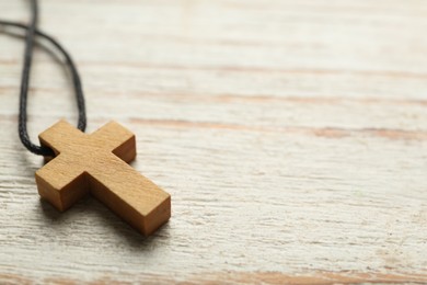 Christian cross on white wooden table, closeup. Space for text