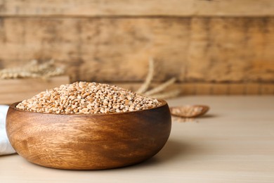 Bowl of wheat grains on white wooden table, closeup. Space for text
