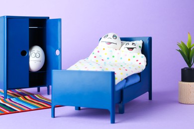 Small bed with couple of eggs and lover hiding in closet on lilac background