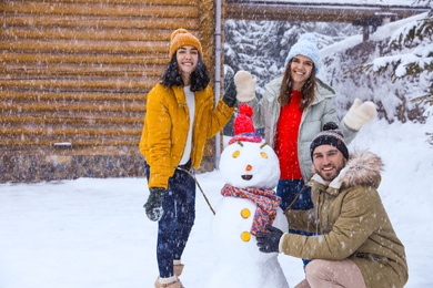 Happy friends with snowman outdoors on snowy day. Winter vacation