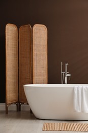 Modern ceramic bathtub and folding screen near brown wall in room