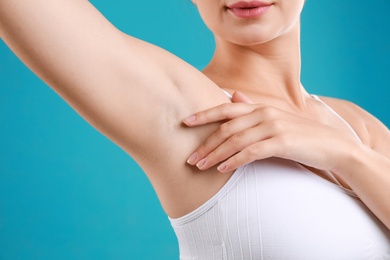 Young woman with smooth clean armpit on teal background, closeup. Using deodorant