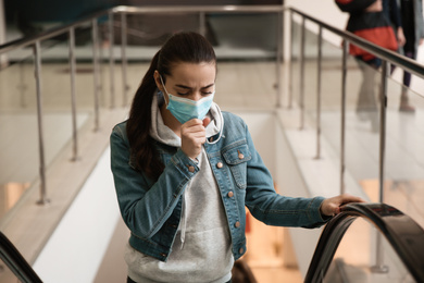 Young woman with disposable mask on escalator in mall. Dangerous virus