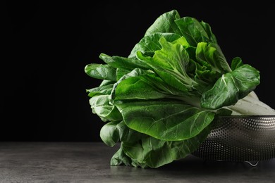 Fresh green pak choy cabbages with water drops in sieve on grey table. Space for text