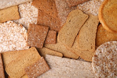 Fresh rye crispbreads, crunchy rice cakes and rusks as background, flat lay