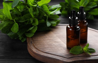 Bottles of mint essential oil and green leaves on black wooden table