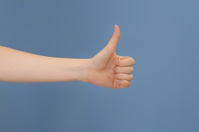 Woman showing thumb up on pale blue background, closeup