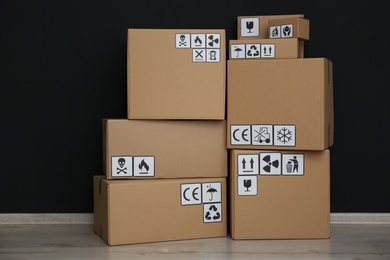 Cardboard boxes with different packaging symbols on floor near black wall. Parcel delivery