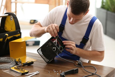 Professional technician repairing electric fan heater with screwdriver at table indoors