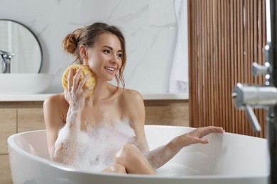 Beautiful woman with sponge taking bath indoors