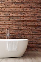 Modern ceramic bathtub with towel near brick wall