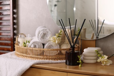 Aromatic reed air freshener, rolled towels and spa stones on wooden table indoors