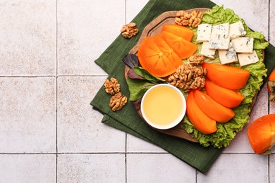 Photo of Delicious persimmon, blue cheese, nuts and honey served on tiled surface, flat lay. Space for text