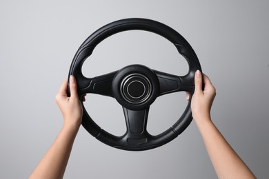 Woman holding steering wheel on grey background, closeup
