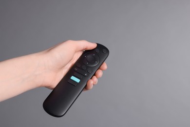 Woman holding TV remote control on grey background, closeup. Space for text