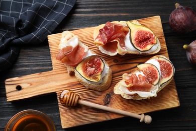 Sandwiches with ripe figs, prosciutto and cream cheese served on black wooden table, flat lay