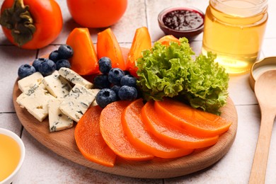 Photo of Delicious persimmon, blue cheese and blueberries on tiled surface, closeup