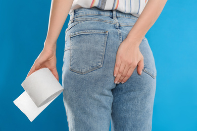 Woman with toilet paper suffering from hemorrhoid on light blue background, closeup
