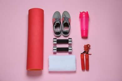 Exercise mat, dumbbells, towel, skipping rope, shaker and shoes on pink background, flat lay