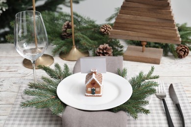 Photo of Festive place setting with beautiful dishware, cutlery and gingerbread house card holder for Christmas dinner on white wooden table