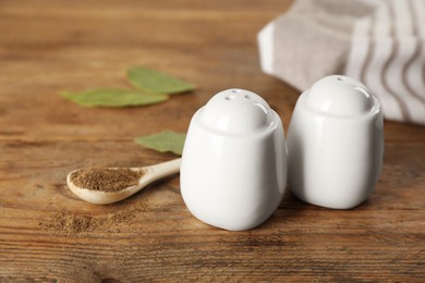 Photo of White ceramic salt and pepper shakers with spoon on wooden table, closeup