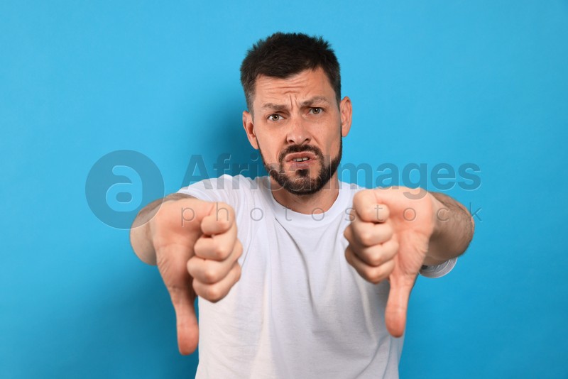 Man showing thumbs down on light blue background