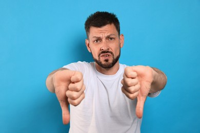Man showing thumbs down on light blue background