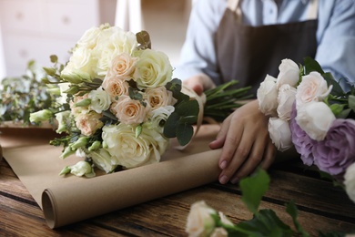 Florist wrapping beautiful wedding bouquet with paper at wooden table, closeup