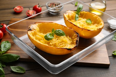 Photo of Halves of cooked spaghetti squash with basil in baking dish on wooden table, closeup
