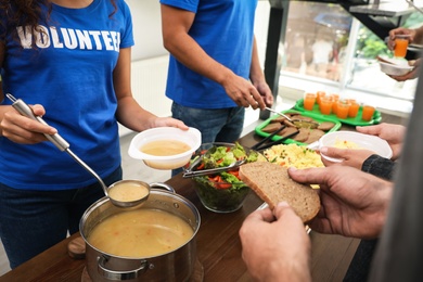 Volunteers serving food to poor people in charity centre, closeup