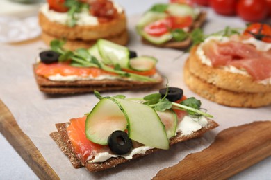 Tasty rye crispbreads with salmon, cream cheese and vegetables on wooden board. closeup