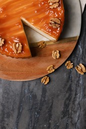 Photo of Delicious cheesecake with caramel and walnuts on black marble table, flat lay. Space for text