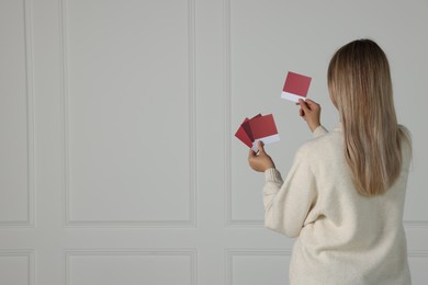 Photo of Woman with color sample cards choosing paint shade for wall indoors, back view. Interior design
