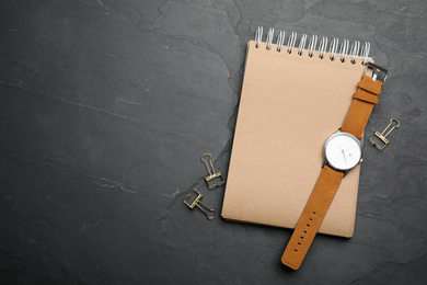 Kraft notebook and stylish wristwatch on black table, flat lay. Space for text