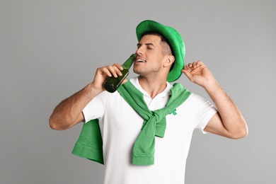 Man in St Patrick's Day outfit drinking beer on light grey background